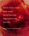 A close-up promotional graphic of a red beverage in a glass with overlaid white text reading: 'Built for modern rituals', 'Ready to pour', 'Natural flavourings', 'Vegan & gluten free', '0.2% ABV', and 'Chilled.